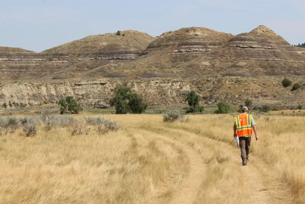 Tom Errico doing a visual services evaluation in Montana field approaching sandy foothills. Photo taken by Visualization Services expert Ryan Mehr-Biggs.